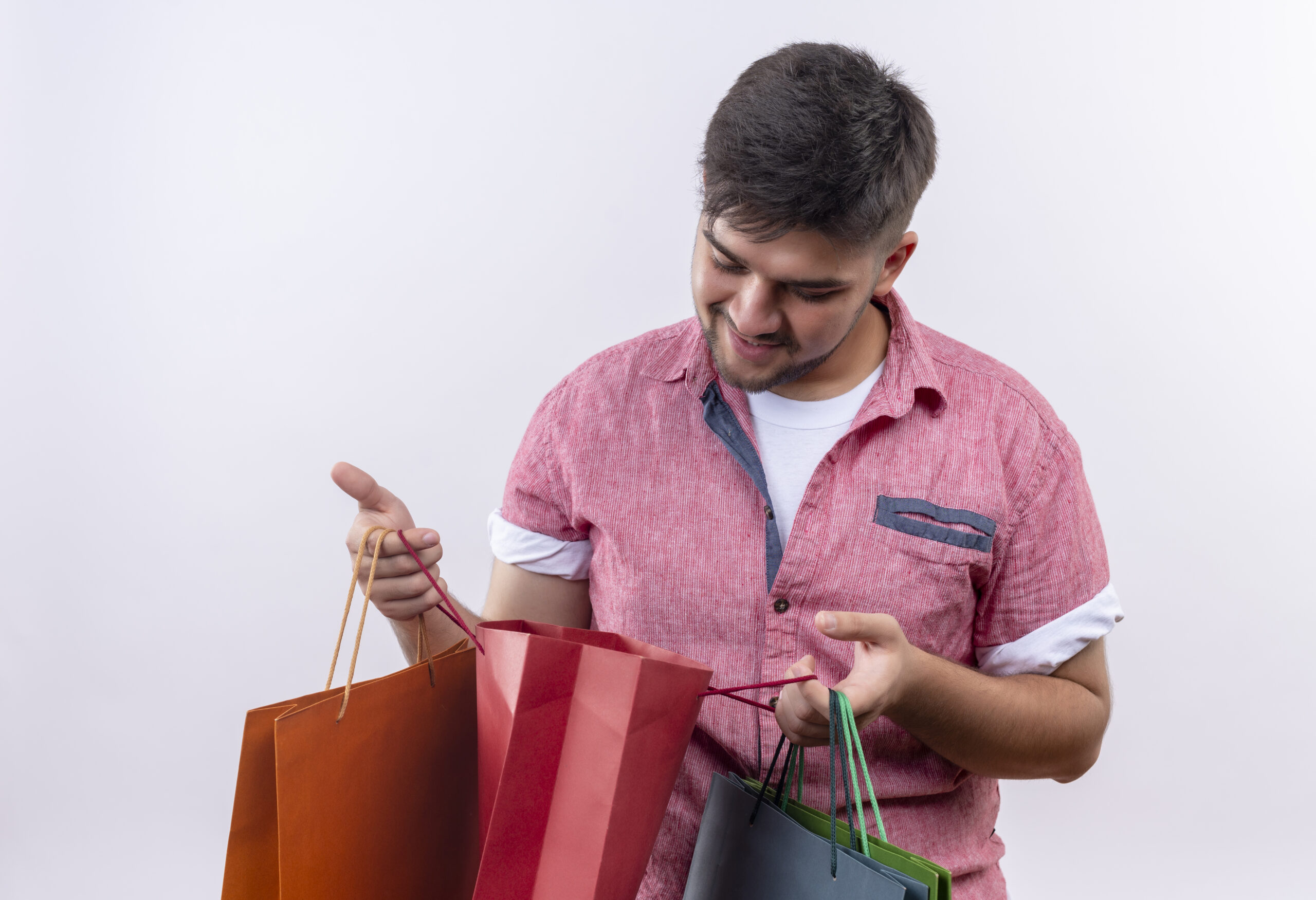 young handsome guy wearing pink polo shirt curiosityly looking in shopping bag standing over white background